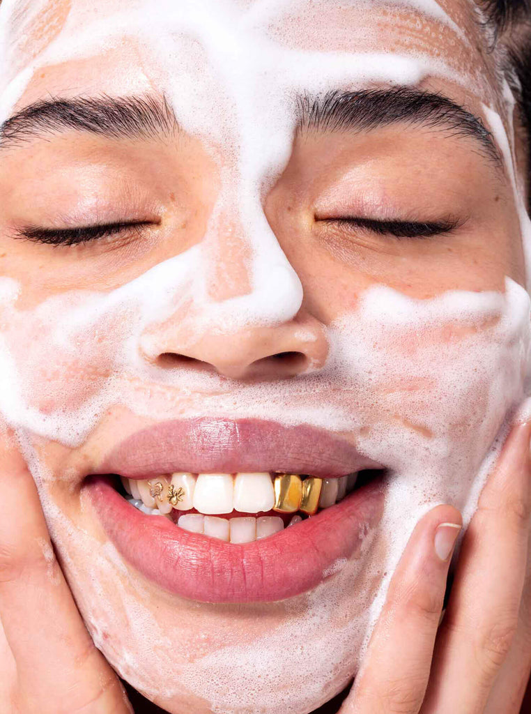 Model with gold teeth washing face with Velvet Cloud cleanser